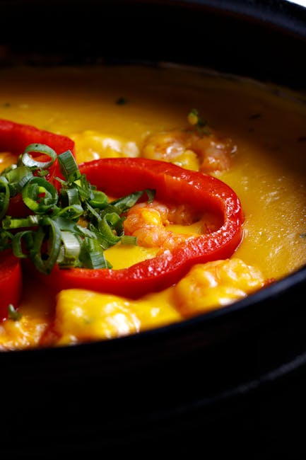 A vibrant shrimp stew with red peppers and creamy sauce, garnished with green onions.