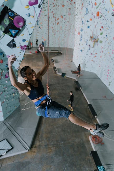 Smiling woman climbs an indoor wall, showcasing skill and enthusiasm.