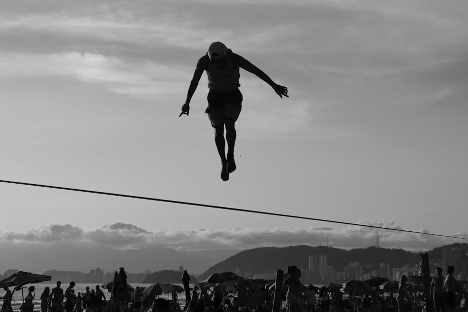 A silhouette of a man skillfully balancing on a tightrope at the beach during sunset.