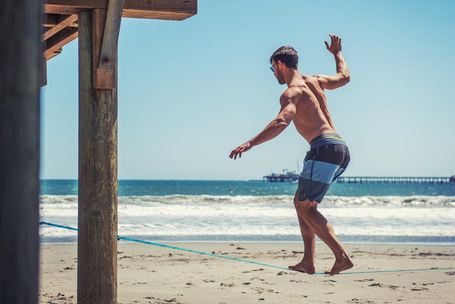 A man skillfully balances on a slackline beneath a wooden pier at Avila Beach on a sunny day.