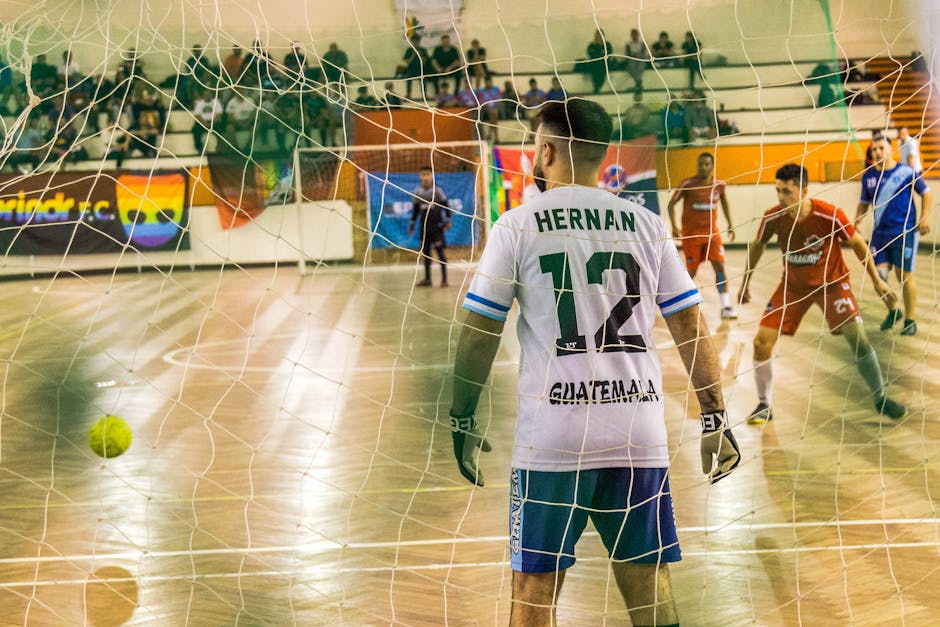 Goalkeeper watches incoming players in an intense indoor soccer match.